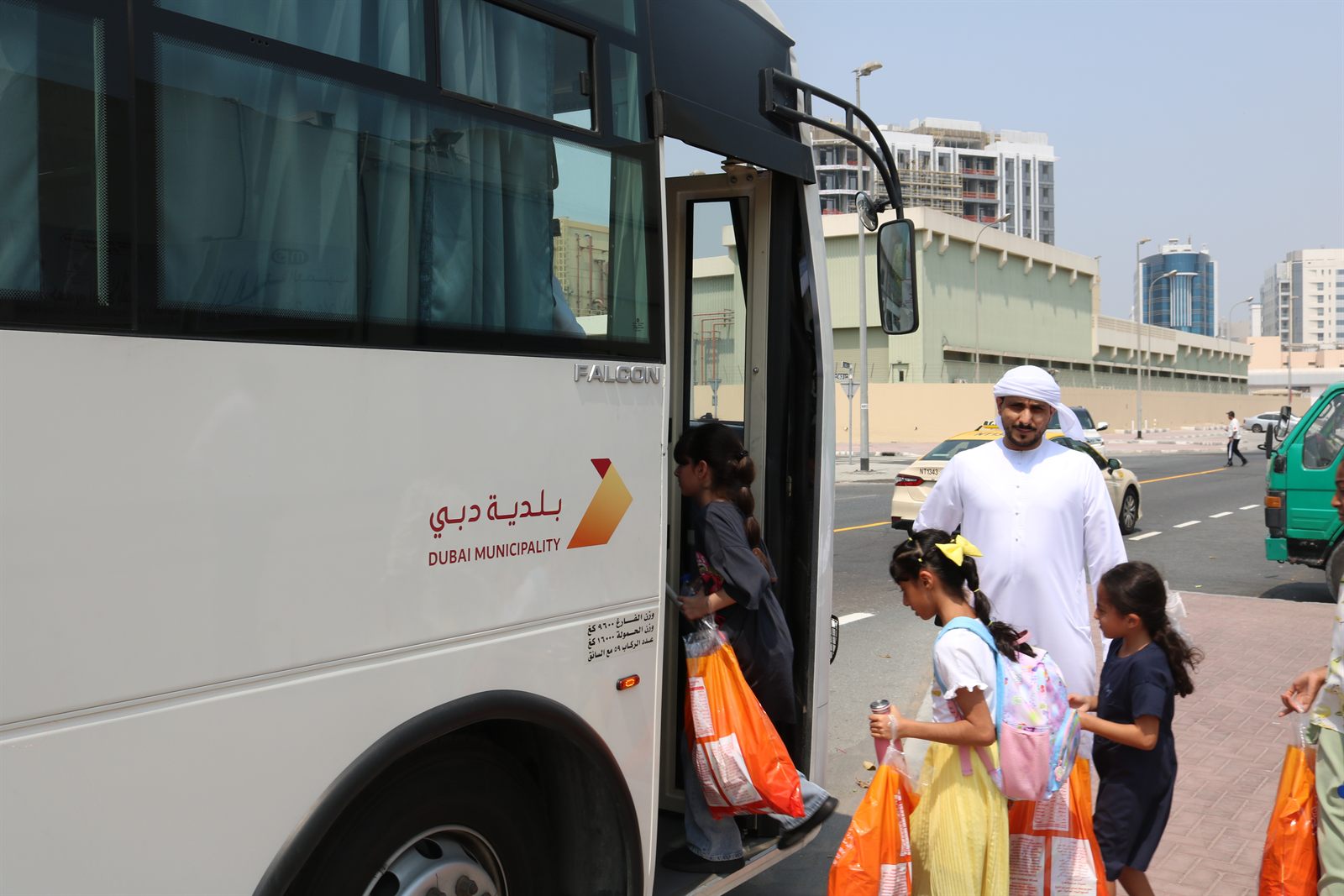 Children collecting Dubai Pofak bags beside a Dubai Municipality bus
