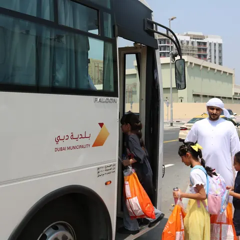 Children collecting Dubai Pofak bags beside a bus